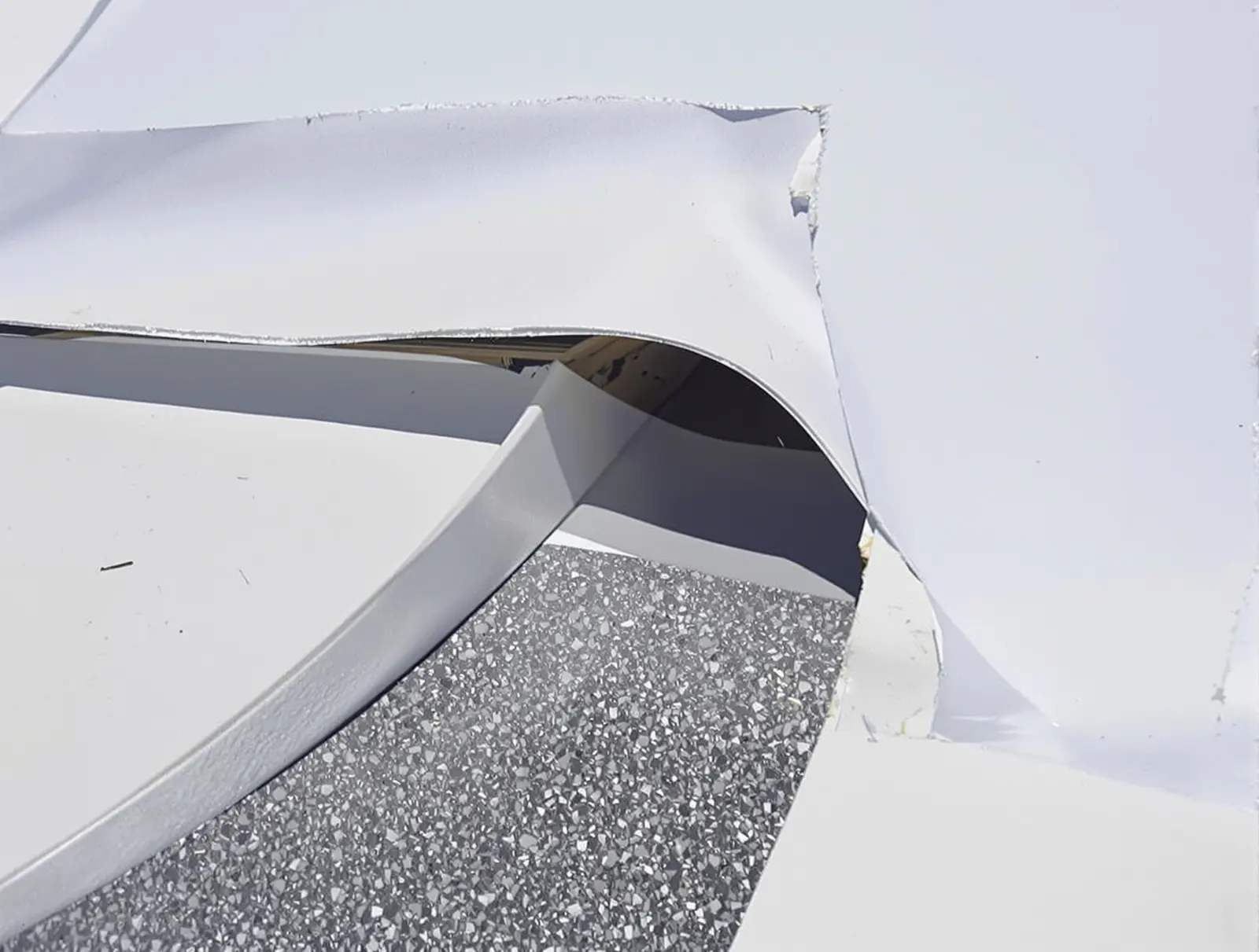 Close-up of a failed seam on a single-ply roofing membrane showing edge lifting and separation